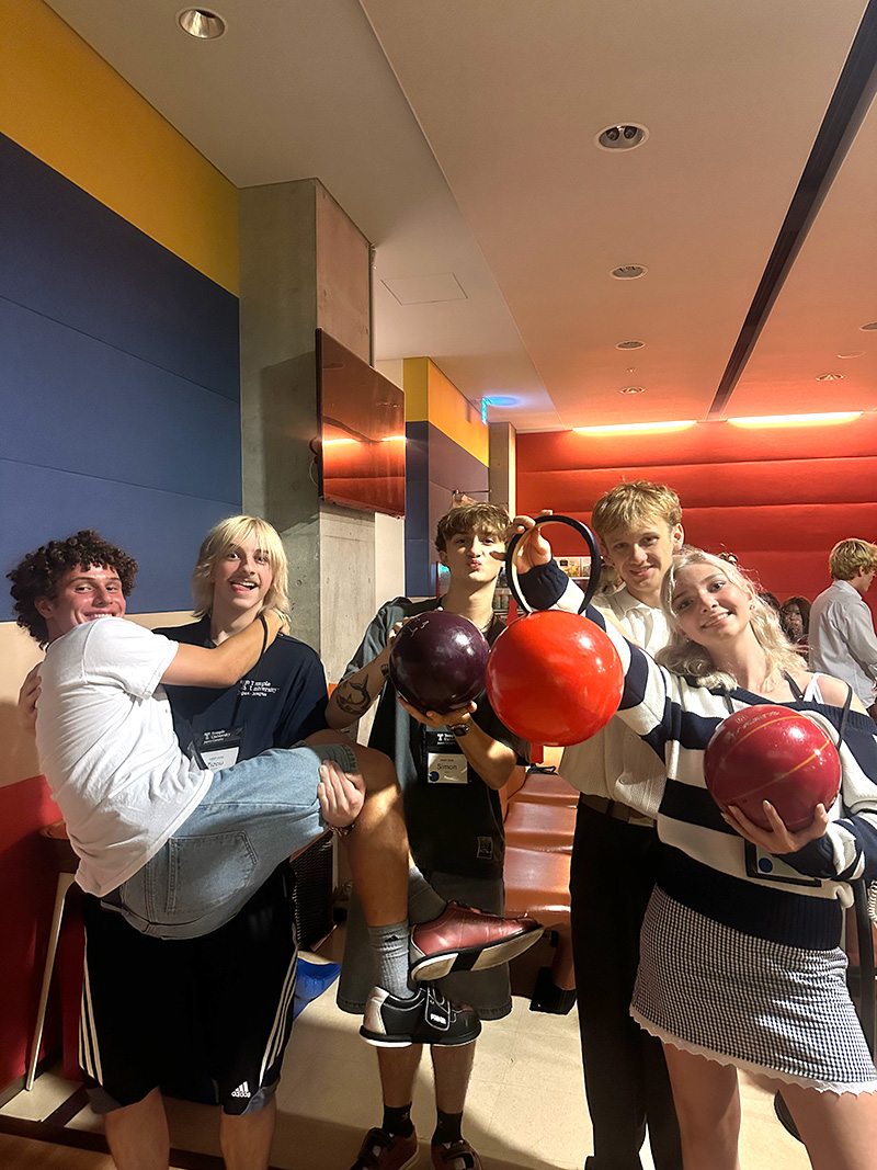 A group of students posing with bowling balls at a bowling alley.